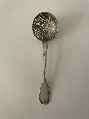 une cuillère en argent ornée d'un motif floral, posée sur une surface blanche