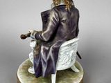 an antique figurine of a man sitting in a chair with a cane