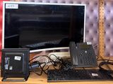 a desk with a monitor, keyboard, phone, and other electronics on it