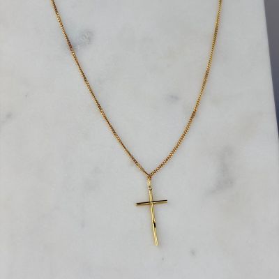 un pendentif en forme de croix en or, suspendu à une chaîne en or, posé sur une surface en marbre