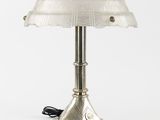 une lampe de table argentée surmontée d'un abat-jour en verre