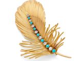 une image représentant une broche en forme de plume, dorée et turquoise, sur fond blanc