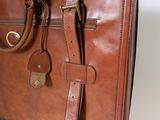 brown leather briefcase sitting on a white surface next to a white wall