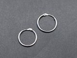 une paire de boucles d'oreilles créoles en argent posées sur une surface noire