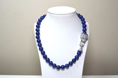 collier de perles bleues orné d'un pendentif en forme de crâne argenté, porté par un mannequin blanc