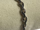 bracelet en argent orné de diamants noirs, posé sur un tissu blanc