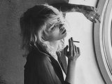 blond woman smoking a cigarette in front of a window with a giraffe sticking its tongue out