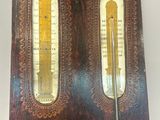 an old wooden clock with two thermometers on it