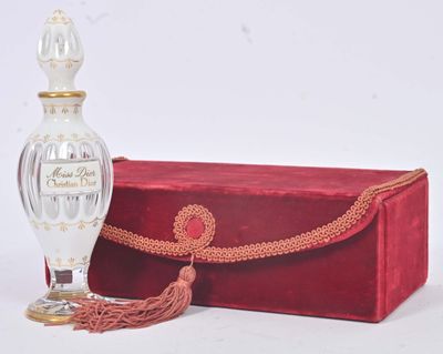 une boîte rouge et une bouteille en verre blanche ornée d'un pompon