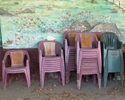 Plusieurs chaises en plastique sont alignées contre un mur, devant un tableau.