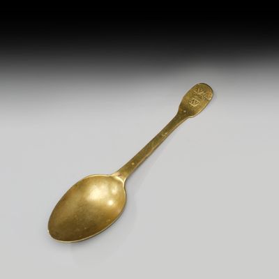 une cuillère en or ancien posée sur une surface blanche, sur fond noir
