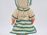 knitted doll sitting on a white pedestal wearing a green and white striped dress