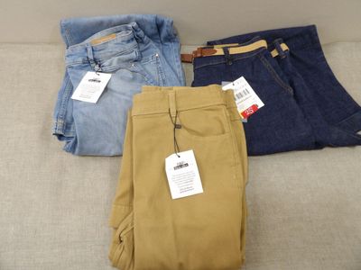 trois paires de pantalons pour homme posées les unes à côté des autres sur un canapé