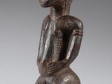 une figurine en bois représentant un homme assis sur un tabouret