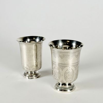 une paire de tasses en métal argenté posées sur une surface blanche, sur fond blanc