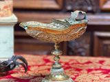un bol en or posé sur une nappe rouge, à côté de quelques coquillages