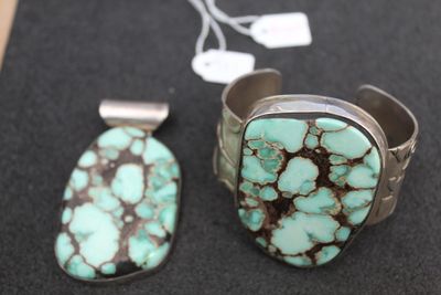 two pieces of turquoise and silver jewelry on a black surface