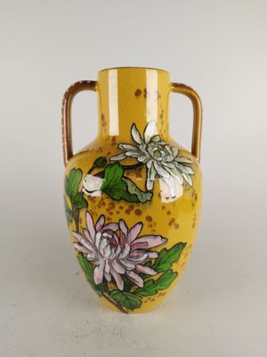 un vase jaune orné de fleurs peintes, posé sur une table