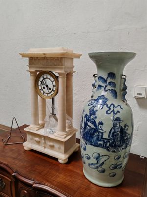 un vase bleu et blanc posé sur une table à côté d'une horloge