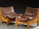 une paire de fauteuils en cuir marron aux pieds en bois, dans une pièce sombre