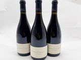 trois bouteilles de vin sont posées sur une surface blanche, devant un fond blanc