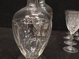 a glass vase with a bird on it next to a wine glass