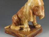 statue d'un chien assis sur un socle en bois, posée sur une surface grise