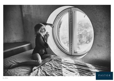 black and white photograph of a woman sitting on a bed in front of a round window