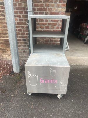 a metal cart with a shelf on it in front of a brick wall