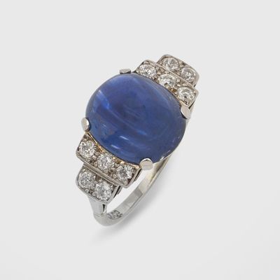 un gros plan d'une bague en pierre bleue et diamants posée sur une surface blanche