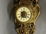 a gold clock hanging on the wall with a bird on it