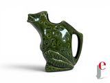 a green vase with a frog on it on a white surface