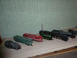 Plusieurs petits trains sont alignés sur une table devant un mur vert.