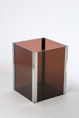 un cube en verre reposant sur un socle métallique, posé sur une surface blanche