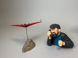 une figurine représentant un homme assis sur un rocher à côté d'un petit avion