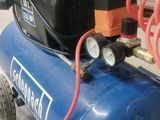 a blue air compressor sitting on the floor next to a red hose