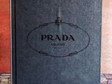 un livre Prada noir posé sur un sol carrelé