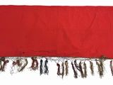 a red blanket with fringes on it on a white surface