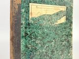 an old book with a green cover sitting on top of a white surface