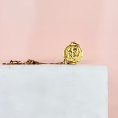 a gold necklace with a coin on it sitting on top of a marble block