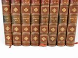six old books are lined up in a row on a white surface