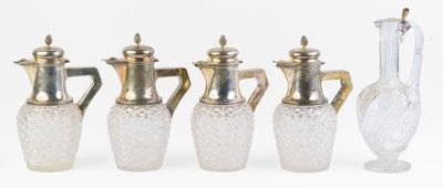 quatre vases en verre et un vase en argent posés sur une surface blanche