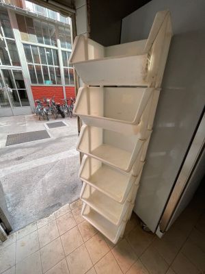 a stack of white shelves next to a refrigerator in a room