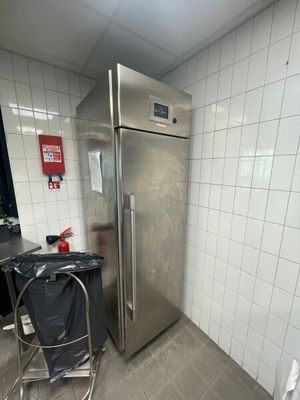 un réfrigérateur en acier inoxydable dans une cuisine, avec une poubelle placée devant