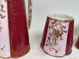 a pink and gold pitcher and two cups on a white table