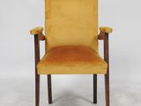 a yellow chair with wooden legs and arm rests against a white wall