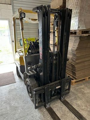 un chariot élévateur dans un entrepôt, avec des piles de bois en arrière-plan
