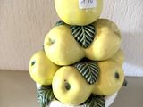 des pommes jaunes dans un bol blanc, accompagnées de feuilles vertes, posées sur une table
