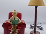 a figurine of a man sitting in a chair reading a book