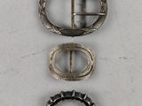 three silver buckles and a silver ring on a white surface